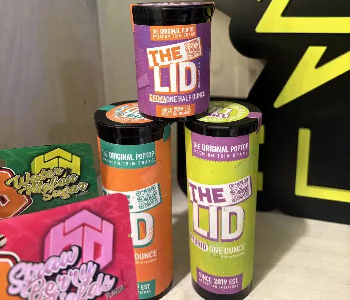 Colorful cannabis containers labeled 'THE LID' in various strains and sizes, from The Original Poptop brand